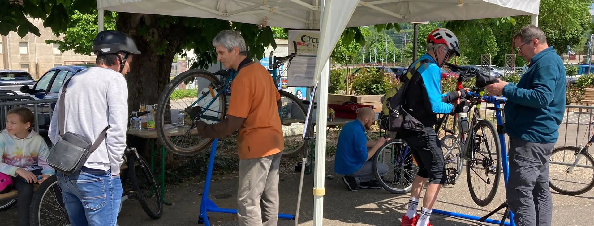 Un atelier mobile installé sous barnum, deux vélos sur pieds de réparation et plusieurs personnes autour.