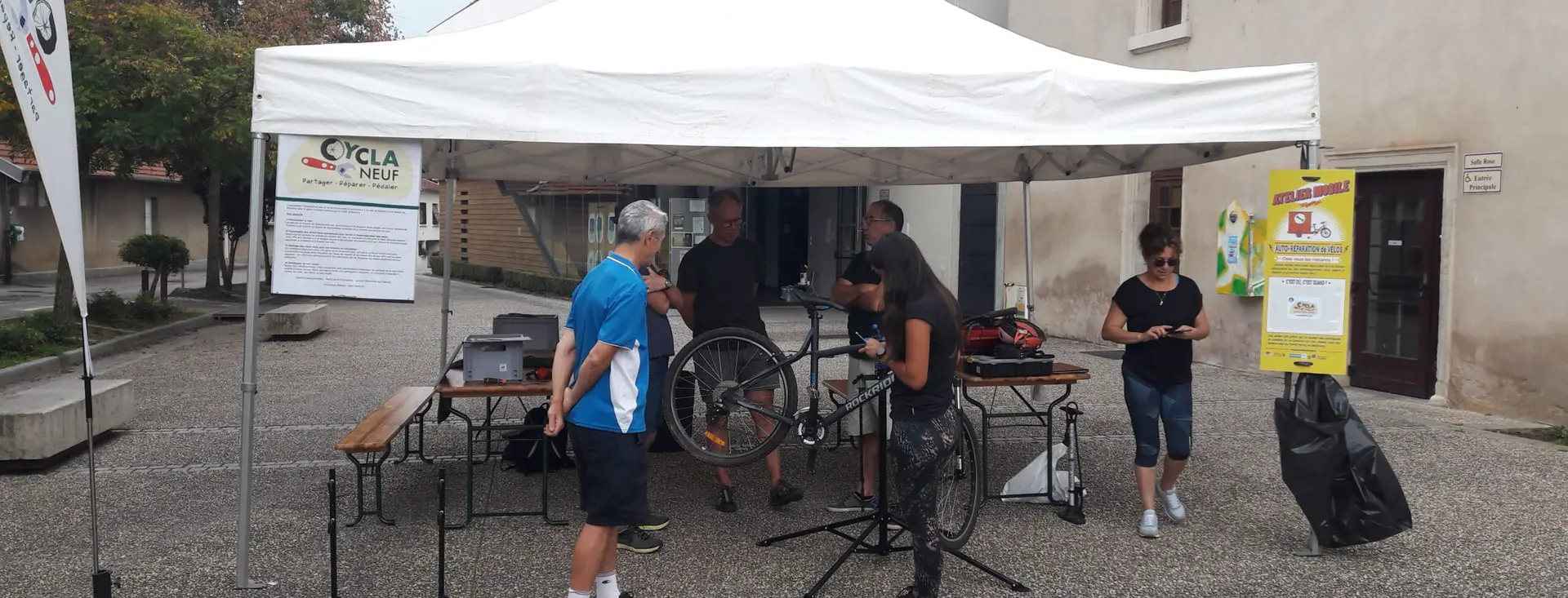 Un stand de réparation de Cyclaneuf installé en extérieur, plusieurs vélos en attente.