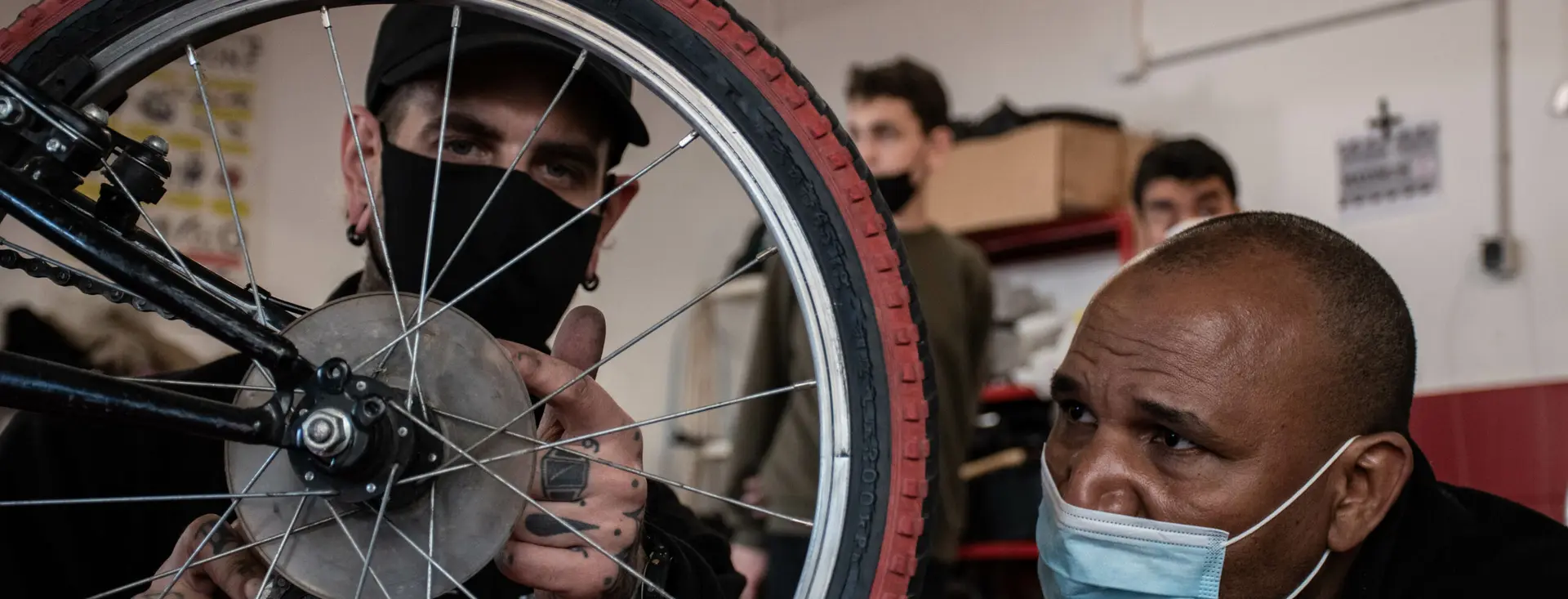 Un bénévole de Cyclo’Minus rayonne une roue devant deux personnes qui regardent faire.