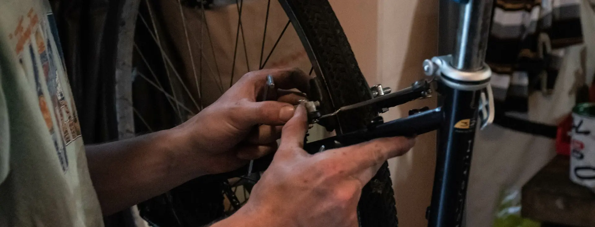 Une main serre l’écrou d’une roue à la clé plate, sur un vélo au pied de réparation.